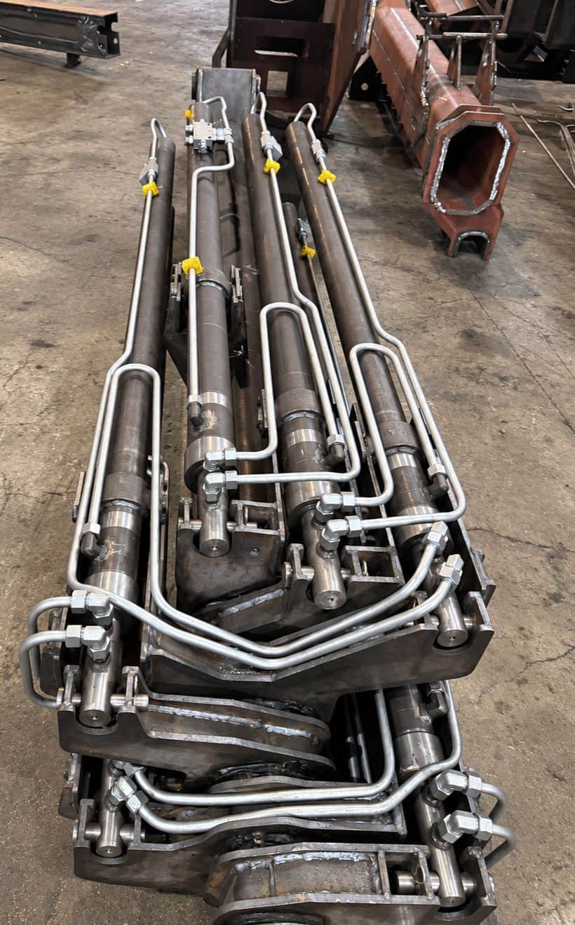 Hydraulic cylinders mounted on mobile crane boom mechanism — custom bent steel piping installation and manifold block designed by AEB Engineering